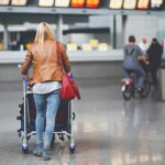 woman in leather coat pushing suitcases in airport terminal