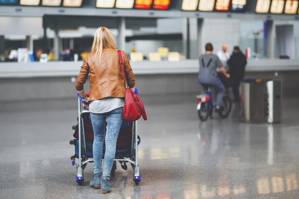 woman in leather coat pushing suitcases in airport terminal