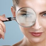 Woman with beautiful skin looking through a magnifying glass.