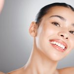 Portrait of woman with beautiful skin holding up two finders.